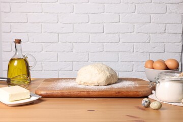 Fresh dough sprinkled with flour and other ingredients on wooden table near white brick wall