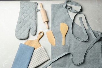 Kitchen napkins, apron and different utensils on light grey table, flat lay