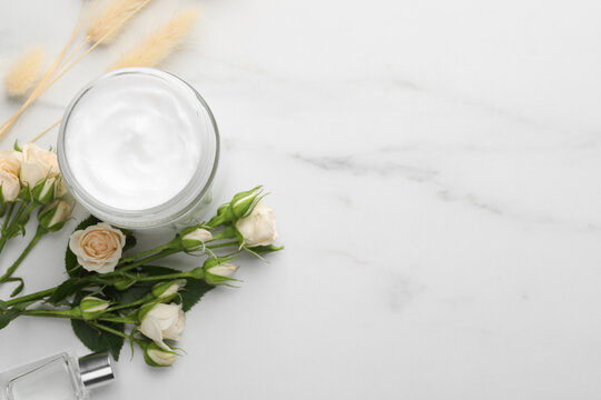 Jar of hand cream and roses on white marble table, flat lay. Space for text