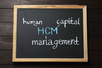 Obraz premium Small blackboard with abbreviation HCM (Human Capital Management) on wooden background, top view