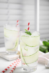 Glasses of refreshing cucumber water with basil on white table