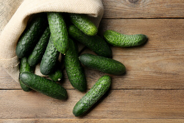 Fresh ripe cucumbers in sack on wooden table, flat lay. Space for text