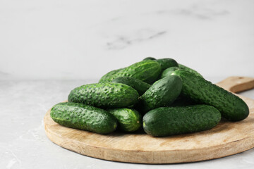Board with fresh ripe cucumbers on white marble table