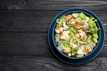 Bowl of delicious cucumber salad on black wooden table, top view. Space for text