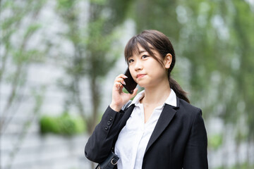 屋外でスマートフォンを使うスーツ姿の若い女性