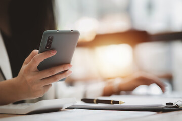 Beautiful Asian woman playing mobile phone in her break from work, she is a marketing manager of a startup company, female leader, supervisor, ceo. Female Leadership Concept.