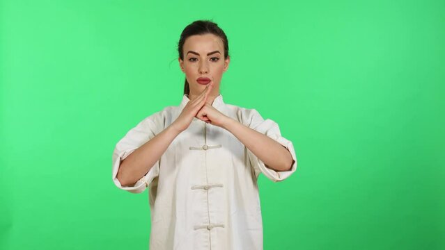 Young caucasian woman in white kungfu wushu uniform practicing martial arts and salutation while looking in camera. Green screen for chroma key in background