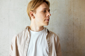 Portrait of caucasian blond man standing on gray textured wall in casual clothes looking aside with thoughtful facial expression. Indoor picture of confident smart male posing on studio background