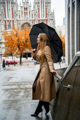 Fototapeta premium blonde woman in beige coat with black umbrella walking on the street in the Kyiv city in autumn