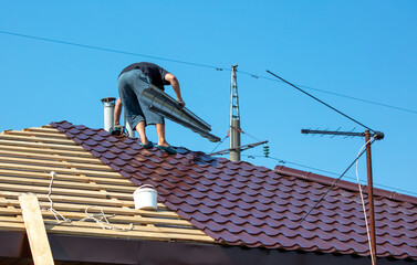Workers install metal roofing on the wooden roof of a house.