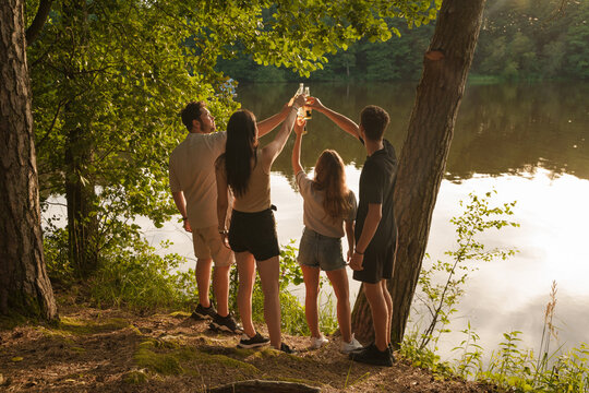 Shot Of Two Guys And Two Girls On Weekend Drinking Beer In Beautiful Summer Wood.