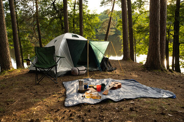 Shot of tourist tent with food and drink on rug in summer wood in daytime.