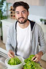 Fototapeta premium glad young bearded man standing at kitchen and preparing salad