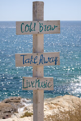 View of wooden signs for Take away, Cold brew, Live music and the sea in the background on the...