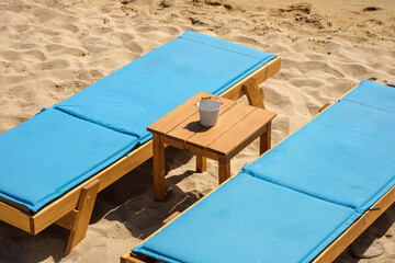Closeup view of two blue sunbeds and a small table in front of the beautiful golden sandy beach of...