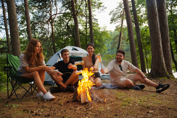 Phootography of friends hikers with tent and marshmallows relaxing together in forest journey.