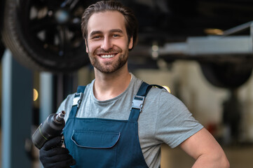 Joyful young car mechanic holding a work tool