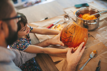 Little girl and her father holding a Halloween pumpkin - obrazy, fototapety, plakaty