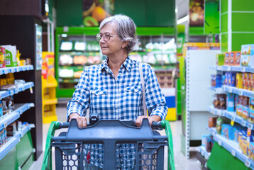 Senior woman at the supermarket pushing cart - concept of consumerism, inflation, rising prices