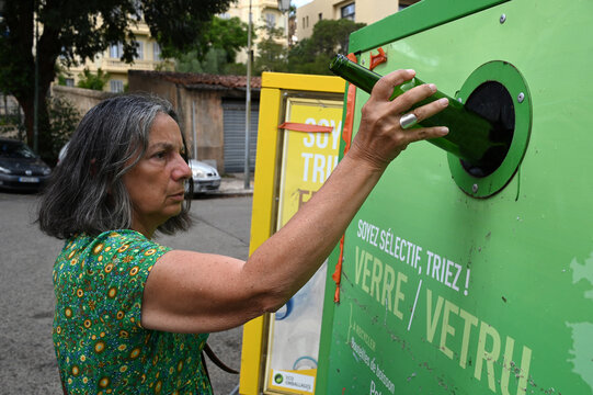 Woman putting a bottle in a glass recycling bin in the city of Ajaccio | Femme mettant une bouteille dans un bac de recyclage du verre de la ville d'Ajaccio