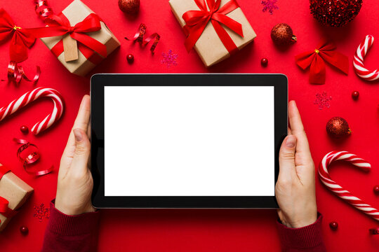 Christmas online shopping from home, female hands holding tablet pc with blank white display top view. woman hand holding tablet with blank screen, Christmas tree and gifts on background