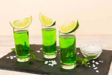 Sweet refreshing mint liqueur, with ice and mint leaves on table background, Shots with lime slice and mint flat lay