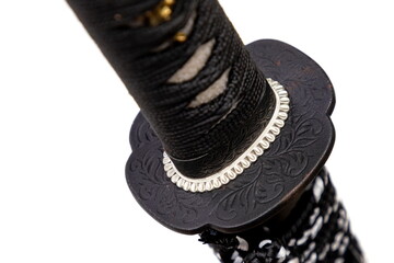 Close up shot of Tsuba - hand guard of Japanese sword made by steel isolated in white background. The sword handle wrapped by black silk cord and white ray skin. Selective focus.