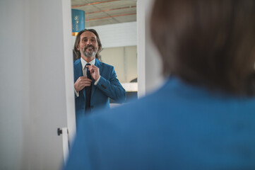 Bearded mature man getting dressed at the mirror