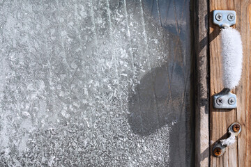Ice patterns on the glass with an icy frost-covered window handle with copy space.  Frozen old wooden window close-up.