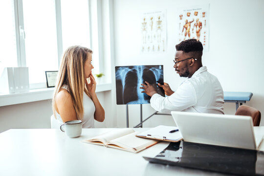 The doctor is analyzing and clarifying images of the patient's lung X-rays. Doctor showing female patient x-ray shot in clinic office. Coronavirus chest X-ray. 