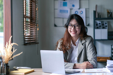 Pretty Asian woman sitting in the office, calculator, working on data, charts and documents on the table in business workspace. Looking camera.