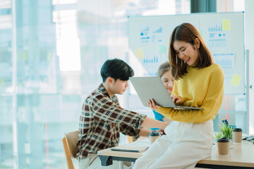 Obraz premium Asian creative teams sit and work together to share inspirational creativity in a workshop. Young modern businessmen are meeting with graph paper and laptop in the workplace.