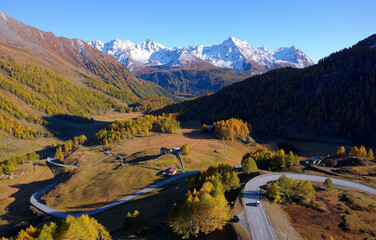 Scenery of beautiful Bernina Pass on a brisk fall day, with a highway winding thru golden larch...