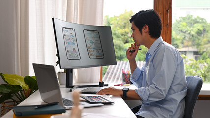 Concentred asian man developer working on mobile application software design project at modern...