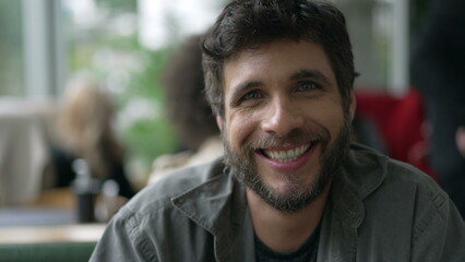 Obraz premium Portrait of a Brazilian young man sitting at coffee shop smiling at camera. Closeup 30s person face