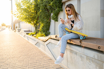 Girl sitting with skateboard and use mobile phone. Outdoors, urban lifestyle. cute skater girl...