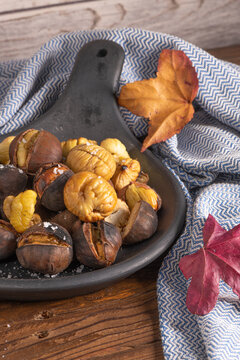 Roasted chestnuts in cast iron pan on an old board