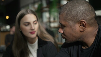 An interracial couple seated at coffee shop talking. Candid people at cafe restaurant in conversation. two people. diversity concept