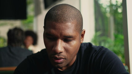 Naklejka premium One young black man in dramatic look seated at coffee shop with contrast shadows by the window