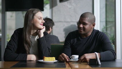 A diverse couple seated at coffee shop in conversation. Two People at cafe place listening and speaking drinking coffee