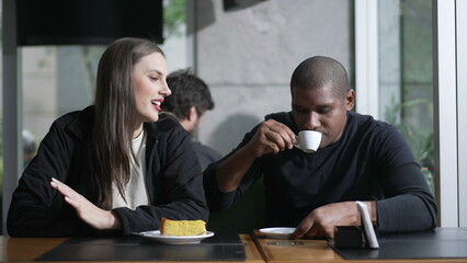 A diverse couple seated at coffee shop in conversation. Two People at cafe place listening and speaking drinking coffee