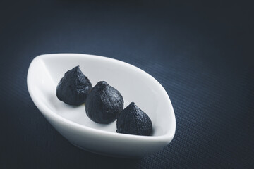 Black garlic in white bowl on black background.