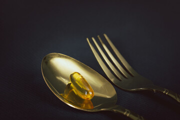 Fish oil in golden spoon on black background.