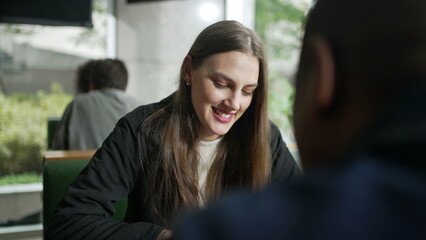 Happy Young woman sitting at coffee shop table in conversation with friend. Smiling person at cafe...