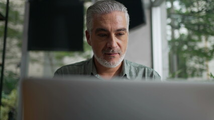 Fototapeta premium Happy older man using laptop computer at coffee shop. Closeup face of a senior entrepreneur looking at screen working remotely at cafe place