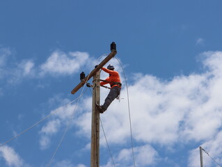 An electrician wearing an orange shirt is installing a new wire on a light pole.