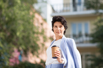 elegant  middle aged business woman  in a suit  drinking coffee while walking in street. Enjoying the little things. Lykke concept. Relaxation Concepts
