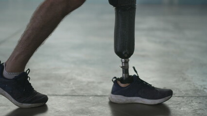 Disabled person walking with his prosthetic leg indoors. Amputee man walks with prosthetic...