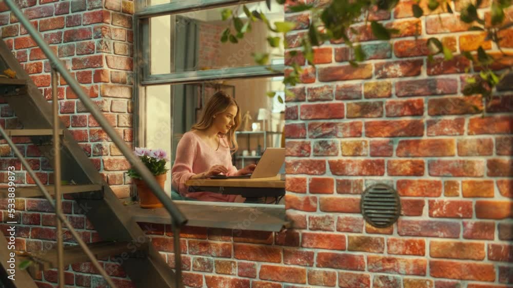 Aufkleber Young Excited Female in Pink Sweater Working on a Laptop Computer while Sitting Behind a Table in Living Room. Business Manager Working Remotely from Home. View from Outside the Window. Static Shot.