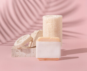 Soap bar with blank label and loofah sponges near stones on light beige close up. Mockup